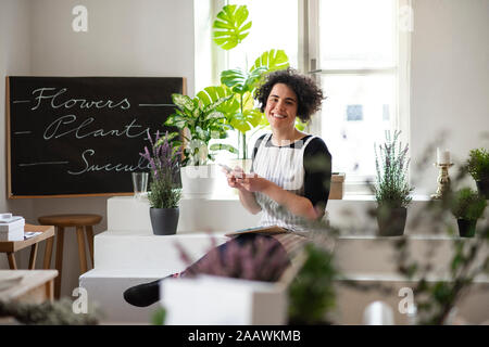 Portrait von lächelnden jungen Frau mit Handy in einem kleinen Laden mit Pflanzen Stockfoto