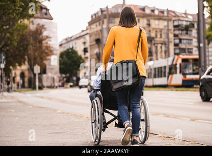 Rückansicht der jungen Frau drücken älterer Mann im Rollstuhl Stockfoto