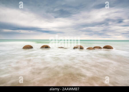 Moeraki Boulders im Meer am Strand gegen Koekohe bewölkter Himmel bei Sonnenuntergang, Neuseeland Stockfoto