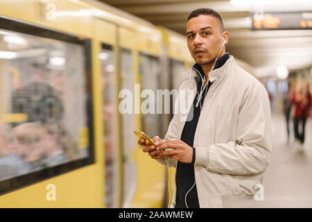 Porträt des Menschen am U-Bahnhof mit Ohrhörer und Handy Plattform, Berlin, Deutschland Stockfoto