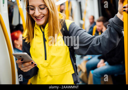 Lächelnde junge Frau, die in der U-Bahn können Sie über Ihr Smartphone Stockfoto