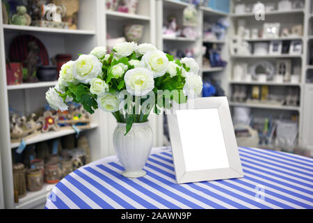 Vorderansicht eines leeren Bilderrahmen Layout und ein Blumenstrauß aus den weißen Rosen in einer Vase. Weiße Blumen auf dem Tisch, die im Hintergrund von Vintage wall. Stockfoto