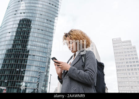 Frau mit Smartphone mit Büro Gebäude im Hintergrund, Berlin, Deutschland Stockfoto