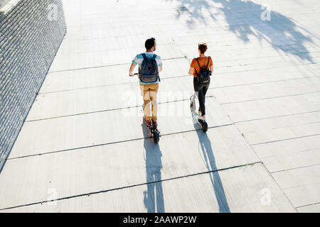 Rückansicht des Paares mit Rucksäcken, Elektroroller Stockfoto