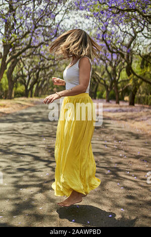 Frau tanzen in der Mitte einer Straße voller Jacaranda Bäume in Blüte, Pretoria, Südafrika Stockfoto