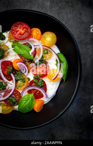 Hüttenkäse mit bunten Cocktail Tomaten, roten Zwiebeln und Pesto Stockfoto