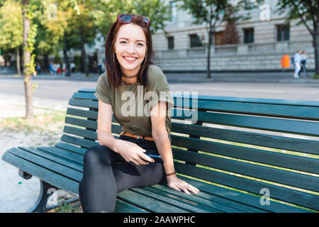 Portrait von lächelnden jungen Frau sitzt auf der Bank mit Smartphone Stockfoto