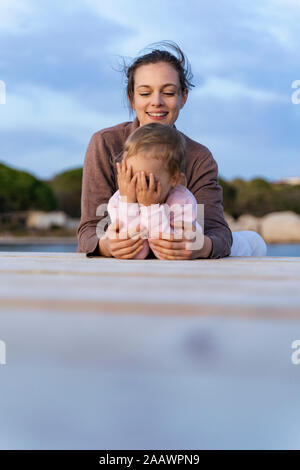 Glückliche Mutter mit Tochter liegen auf einem Steg bei Sonnenuntergang Stockfoto