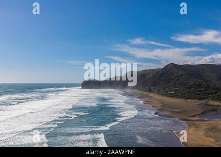 Malerischer Blick auf Klippe von Meer gegen blauen Himmel bei Piha Beach, Auckland, Neuseeland Stockfoto