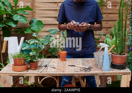 Junger Mann mit Smartphone auf seiner Terrasse bei der Gartenarbeit Stockfoto