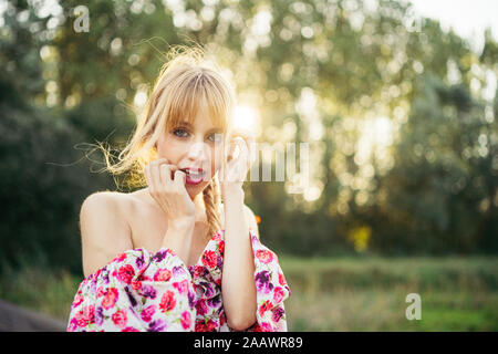 Porträt der blonde junge Frau Sommer Kleid mit Blumenmuster an der Hintergrundbeleuchtung Stockfoto