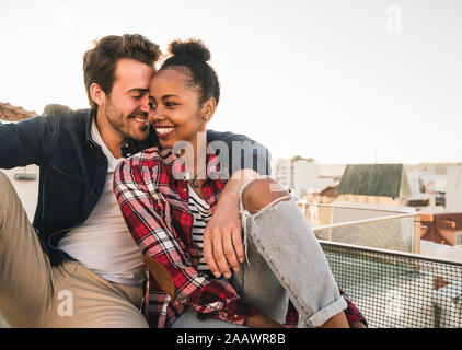 Gerne zärtlich junges Paar sitzen auf der Dachterrasse am Abend Stockfoto