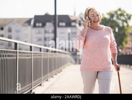 Ältere Frau zu Fuß am Steg, mit Gehstock und Telefonieren Stockfoto