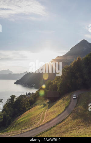 Schweiz, Gersau, Schwyz, Auto fahren entlang der gewundenen Straße bei Sonnenuntergang mit dem Vierwaldstättersee im Hintergrund Stockfoto