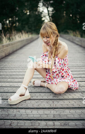 Portrait von überrascht junge Frau sitzt auf der Promenade am Smartphone suchen Stockfoto