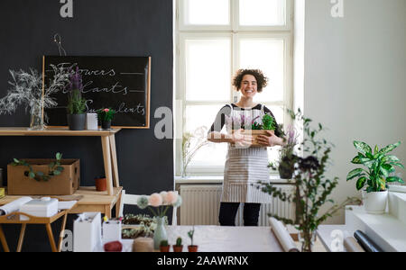 Glückliche junge Frau mit Blumen in einem Karton in einem kleinen Laden Stockfoto