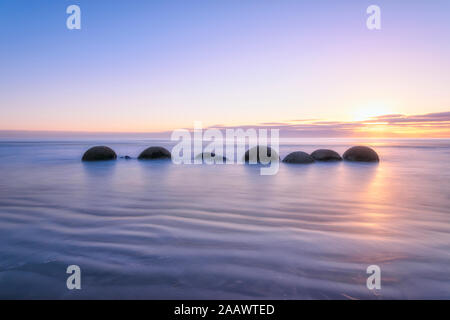 Moeraki Boulders im Meer bei Koekohe Strand gegen Himmel bei Sonnenuntergang, Neuseeland Stockfoto