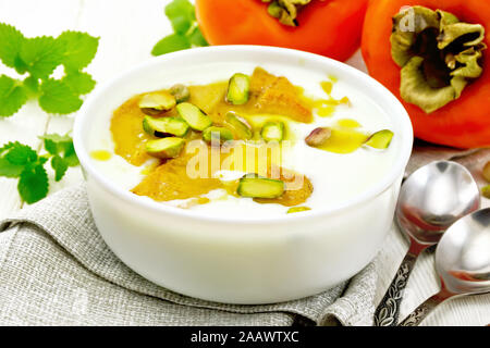 Joghurt, Dattel und Honig Dessert mit Vanille, Kardamom und Pistazien in einer Schüssel auf eine Serviette, Minze und Löffel auf Holzbrett Hintergrund Stockfoto