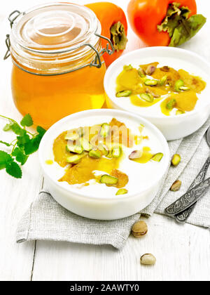 Dessert Joghurt, Dattel und Honig mit Vanille, Kardamom und Pistazien in zwei Schüsseln auf eine Serviette, Minze und Löffel auf dem Hintergrund der hellen Holzmöbeln bo Stockfoto
