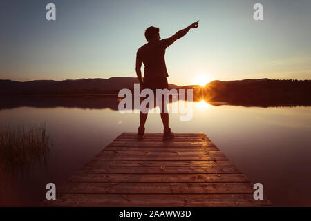 Die Silhouette eines Mannes, der auf den Himmel auf einem Holzsteg bei Sonnenuntergang Stockfoto