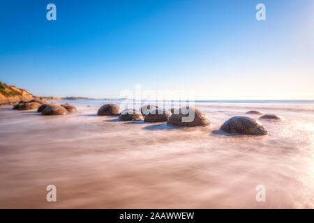 Moeraki Boulders in Meer gegen Himmel an einem sonnigen Tag an Koekohe Beach, South Island, Neuseeland Stockfoto