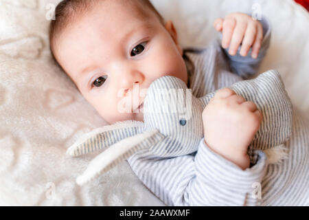 Baby Mädchen liegt auf einer weißen Decke mit Wolken und ein Kaninchen Spielzeug Stockfoto