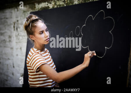 Nachdenkliche junge Frau Zeichnung ein Gedanke bubble auf einer Tafel Stockfoto