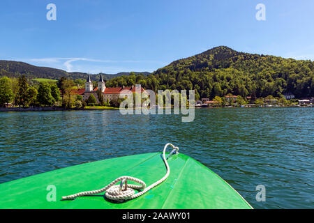 Boot auf See mit Kloster Tegernsee und St. Quirinus Kirche im Hintergrund gegen den blauen Himmel in Bayern, Deutschland Stockfoto