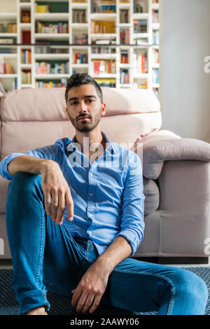 Portrait von ernsthaften jungen Mann auf dem Boden von Wohnzimmer zu Hause sitzen Stockfoto