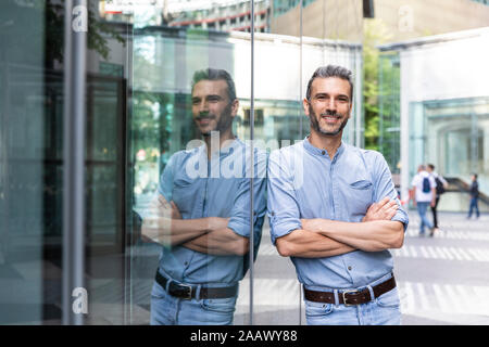 Lächelnd Geschäftsmann mit Reflexion über eine Glasfassade, Berlin, Deutschland Stockfoto