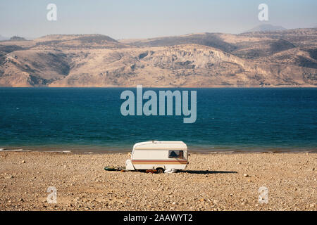 Ein einsamer Wohnwagen am Ufer des Sees zwischen Wüste und Berge geparkt, Usbekistan Stockfoto