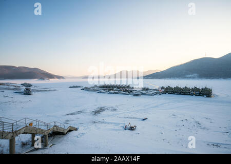 Winterlandschaft von Sonnenuntergang am See Songhua gegen Schnee Berge und zugefrorenen See mit Nebel auf dem See Oberfläche, Provinz Jilin, China Stockfoto