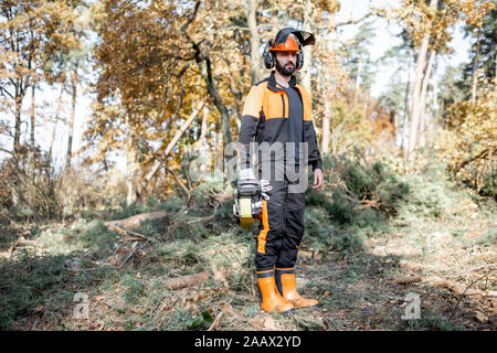 In voller Länge Porträt eines professionellen Holzfäller in schützende Arbeitskleidung stehen mit der Motorsäge im Wald Stockfoto