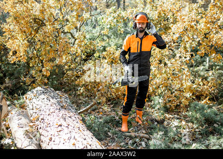 In voller Länge Porträt eines professionellen zuversichtlich lumberman mit Kettensäge in schützende Arbeitskleidung im Pinienwald Stockfoto