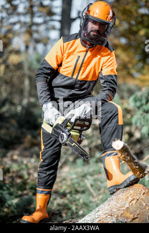 In voller Länge Porträt eines professionellen zuversichtlich lumberman mit Kettensäge in schützende Arbeitskleidung im Pinienwald Stockfoto