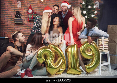 Die Gruppe von fröhlichen alten Freunden ein Geschenk für ein Mädchen. Neues 2019 Jahr kommt. Das neue Jahr in einer gemütlichen Atmosphäre zu Hause feiern. Stockfoto