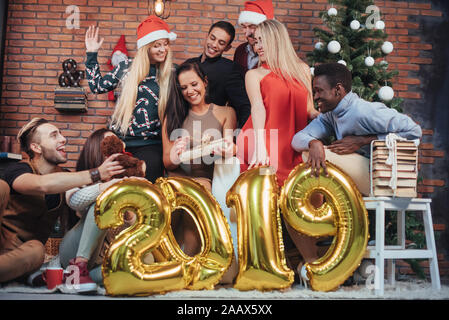 Gruppe von Fröhlichen alte Freunde miteinander kommunizieren. Neues 2019 Jahr kommt. Das neue Jahr in einer gemütlichen Atmosphäre zu Hause feiern. Stockfoto