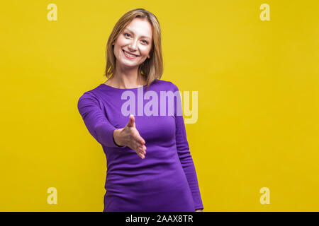 Darf ich mich vorstellen. Portrait von freundliche Frau im eleganten engen lila Kleid Hand, Händedruck, Begrüßung der Gäste mit toothy Lächeln. Stockfoto