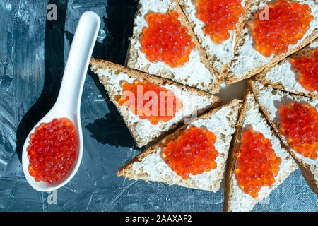 Löffel und Teller mit Schwarzbrot mit rotem Kaviar auf grauem Hintergrund. Roter Kaviar Sandwiches. Gesundes Essen. Stockfoto