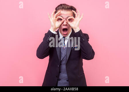 Portrait von überrascht Geschäftsmann im Tuxedo an Kamera durch die Finger in ok Geste suchen, imitieren Gläser oder Fernglas Erschrocken öffnete seine mout Stockfoto