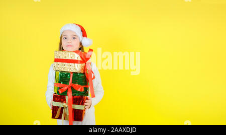 Süße Mädchen in einem santa claus Checker hält Geschenkboxen in bunten Einwickeln von Dokumenten. Gelbe studio Hintergrund. Geschenke Konzept. Stockfoto