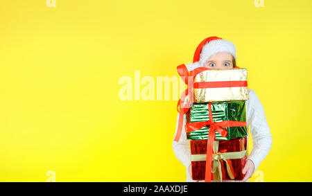 Süße Mädchen in einem santa claus Checker hält Geschenkboxen in bunten Einwickeln von Dokumenten. Gelbe studio Hintergrund. Geschenke Konzept. Stockfoto