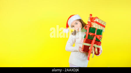 Süße Mädchen in einem santa claus Checker hält Geschenkboxen in bunten Einwickeln von Dokumenten. Gelbe studio Hintergrund. Geschenke Konzept. Stockfoto