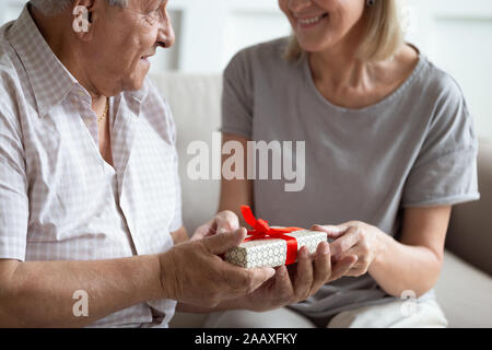 Happy 80 s Mann empfangen verpackte Geschenk von lächelnden reife Frau. Stockfoto