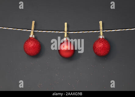 Drei rote Christbaumkugeln hängen von Peg auf einem dunklen Hintergrund mit Glitzer und kopieren Raum Stockfoto