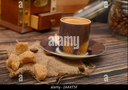 Eine Tasse Kaffee, Stücke von braunem Zucker in einer Schüssel Zucker, Kaffee Bohnen im Glas, eine Kaffeemühle auf einer hölzernen Hintergrund. Nahaufnahme Stockfoto