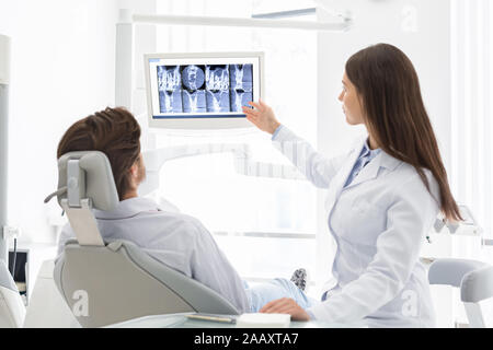 Hübschen weiblichen Zahnarzt erklären, ihre Patienten in Stuhl x-ray Ergebnisse Stockfoto