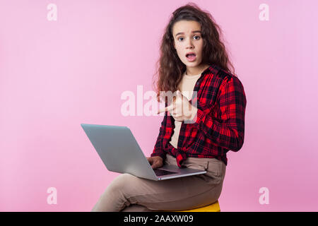 Portrait von frustriert Computer Benutzer, jugendlich Mädchen mit lockigem Brünette Haar in Plaid Shirt at laptop zeigt, auf der Suche über Software Fehler besorgt, Prog Stockfoto