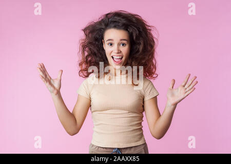 Portrait von verrückt begeisterte Teenager Mädchen mit Zerzausten curly Brünette Haare fliegen und in Freizeitkleidung heben die Hände und schrie vor Freude, ov Stockfoto