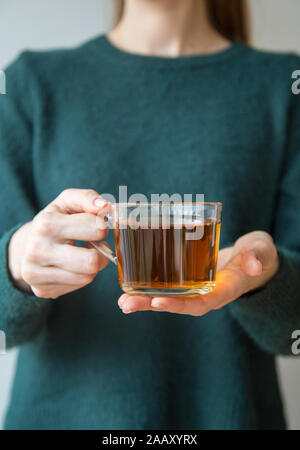 Transparente Tasse Tee in der Hand der Frau im grünen Pullover. Konzept der gemütlichen Platz für Text Stockfoto